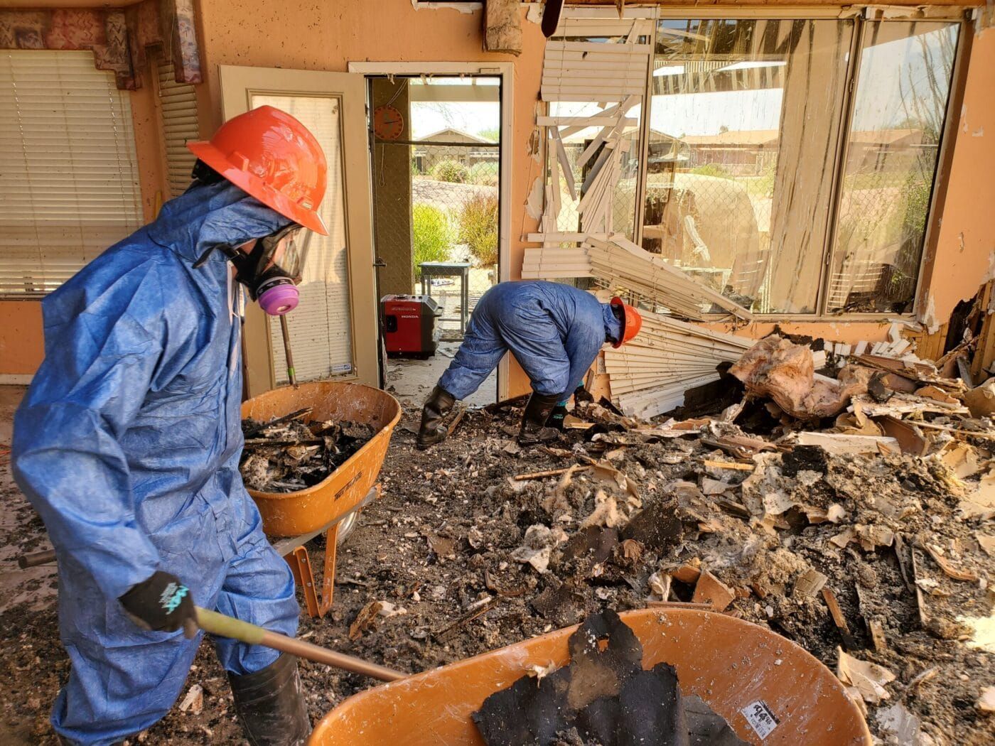 Two men wearing protective suits and hard hats are working on a building.