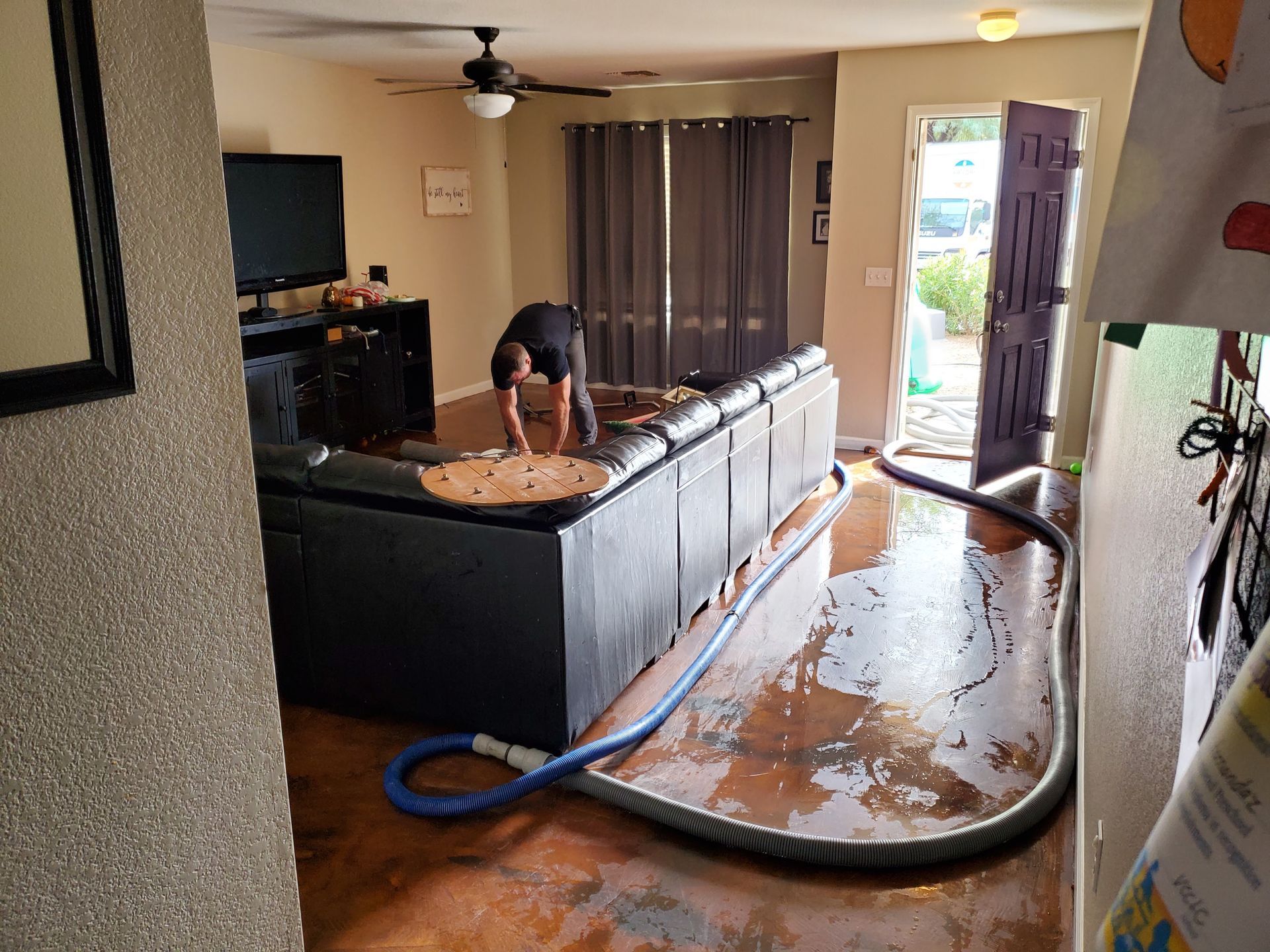 A man is cleaning a flooded living room with a vacuum hose.