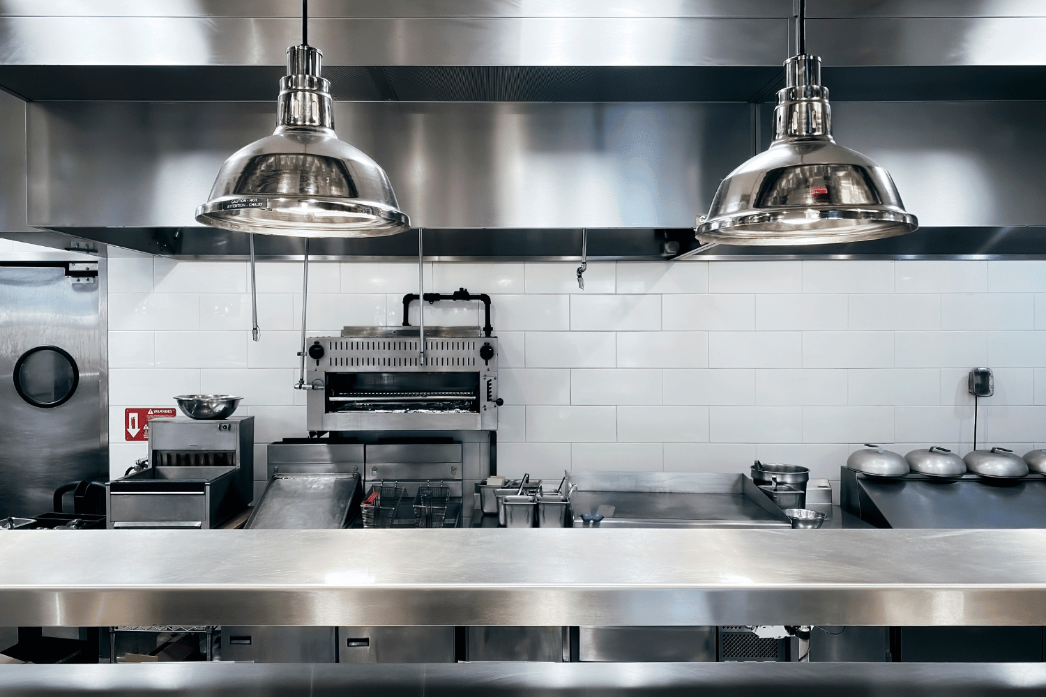 Stainless steel commercial kitchen with industrial lighting and appliances.