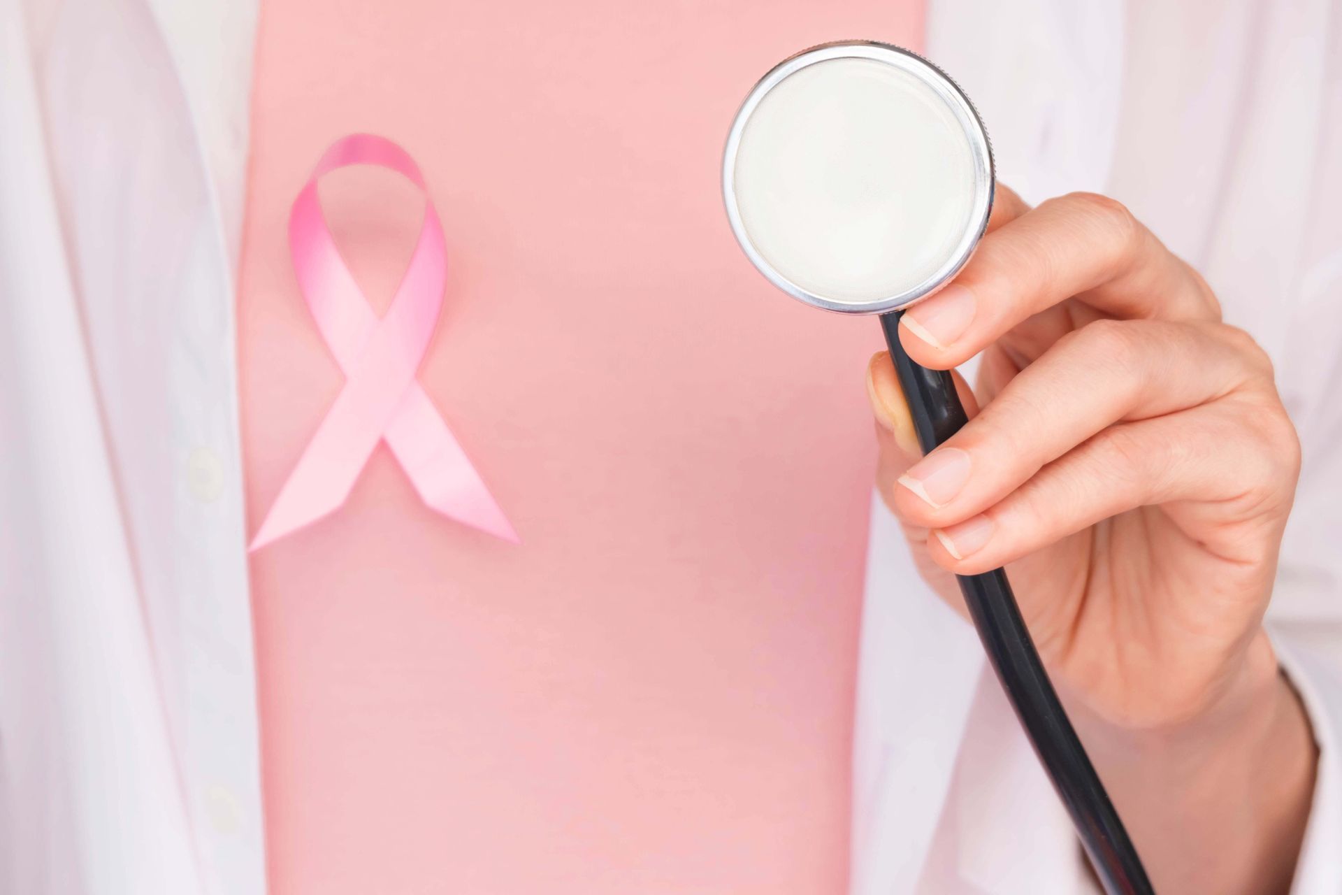 A doctor is holding a stethoscope in front of a pink breast cancer ribbon.