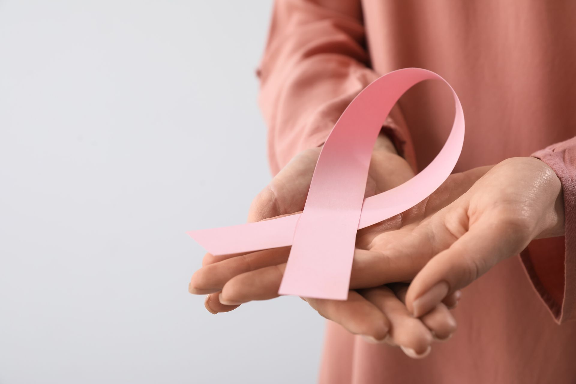 A woman is holding a pink ribbon in her hands.