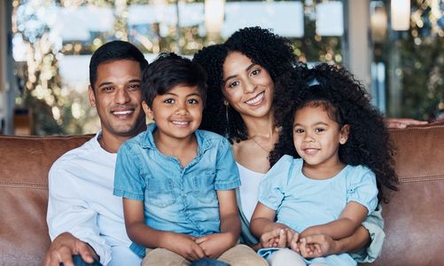 A family is sitting on a couch together and smiling for the camera.