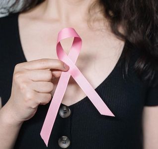 A woman is holding a pink ribbon in front of her chest