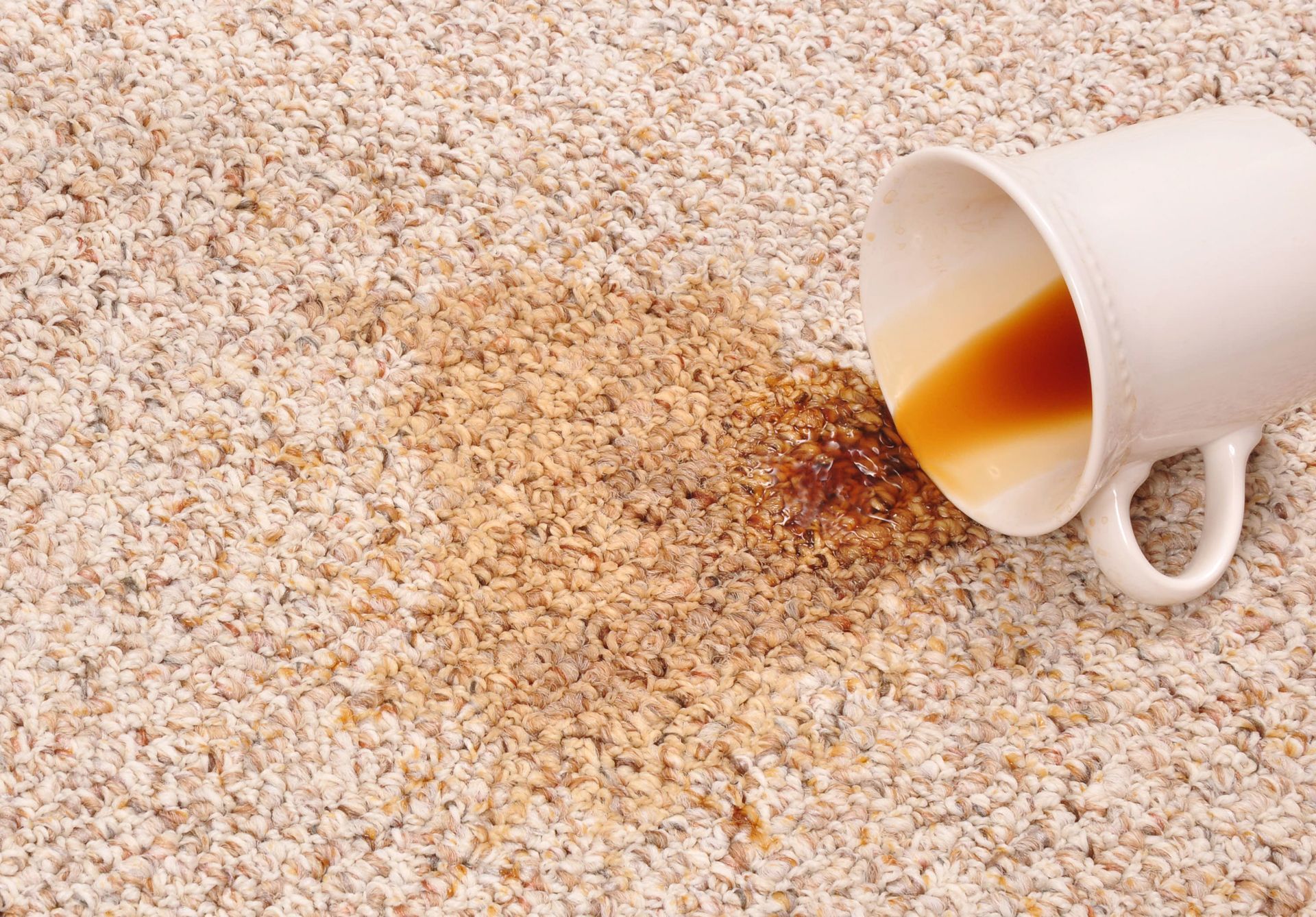 Spilled coffee from a white mug on a bed of beige grains or sand