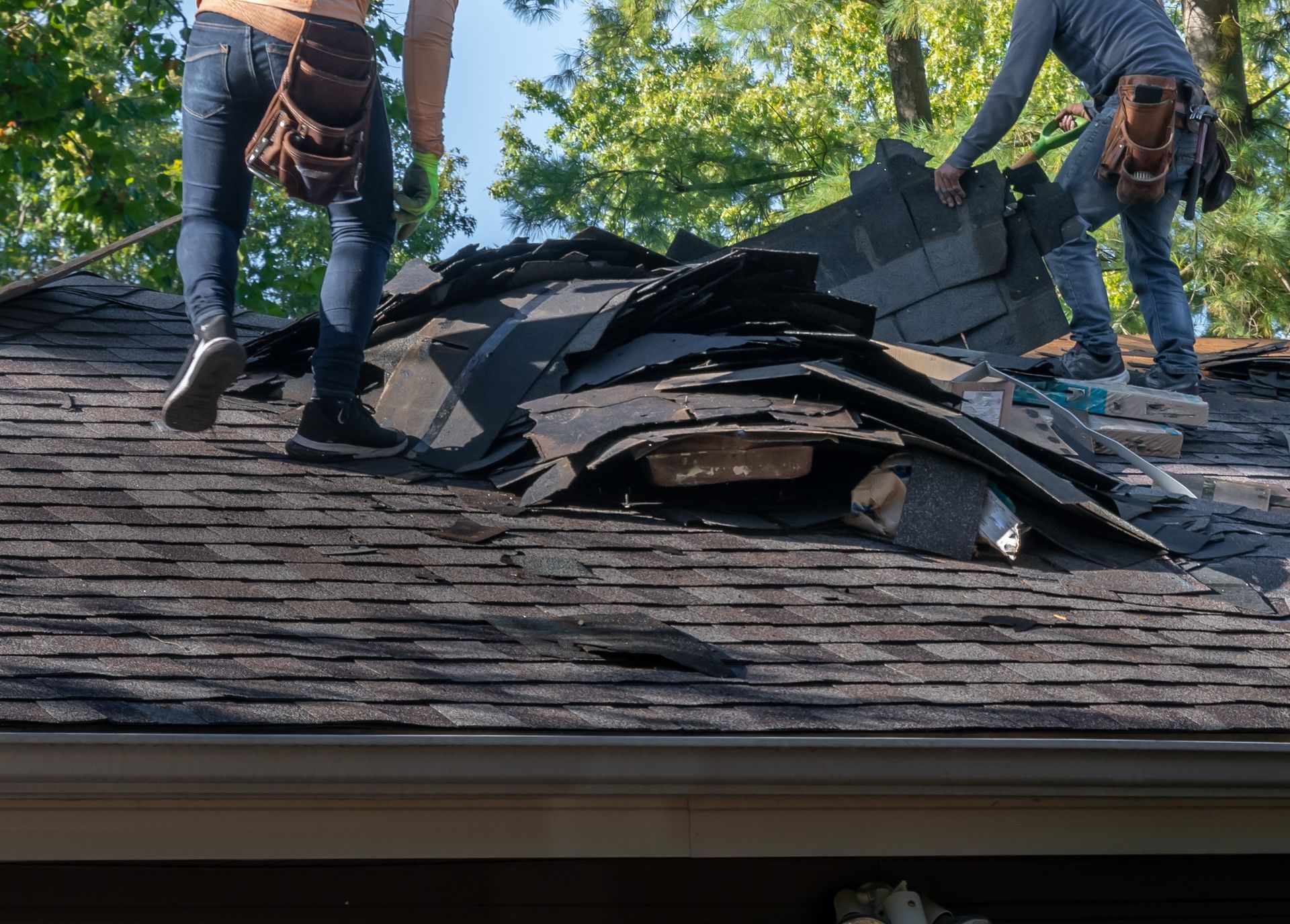 Roofers removing old material from a house in preparation for storm damage repair.