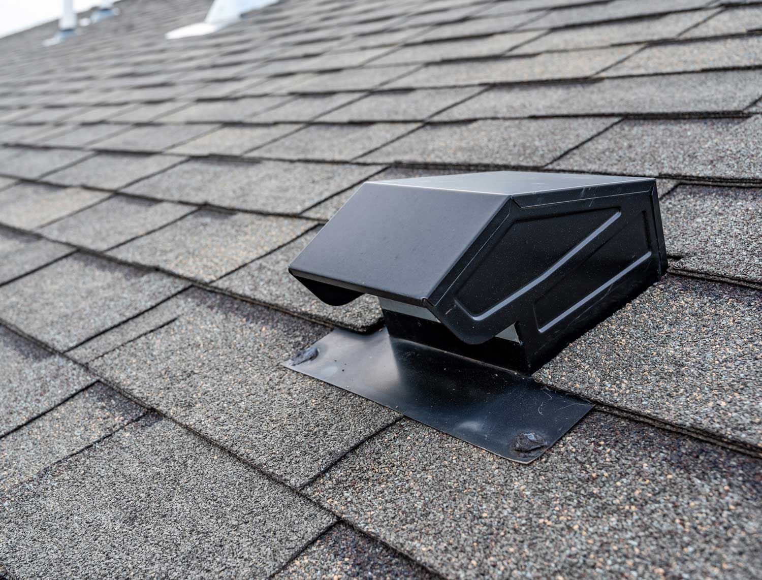 Black roof vent on a gray asphalt shingle roof.