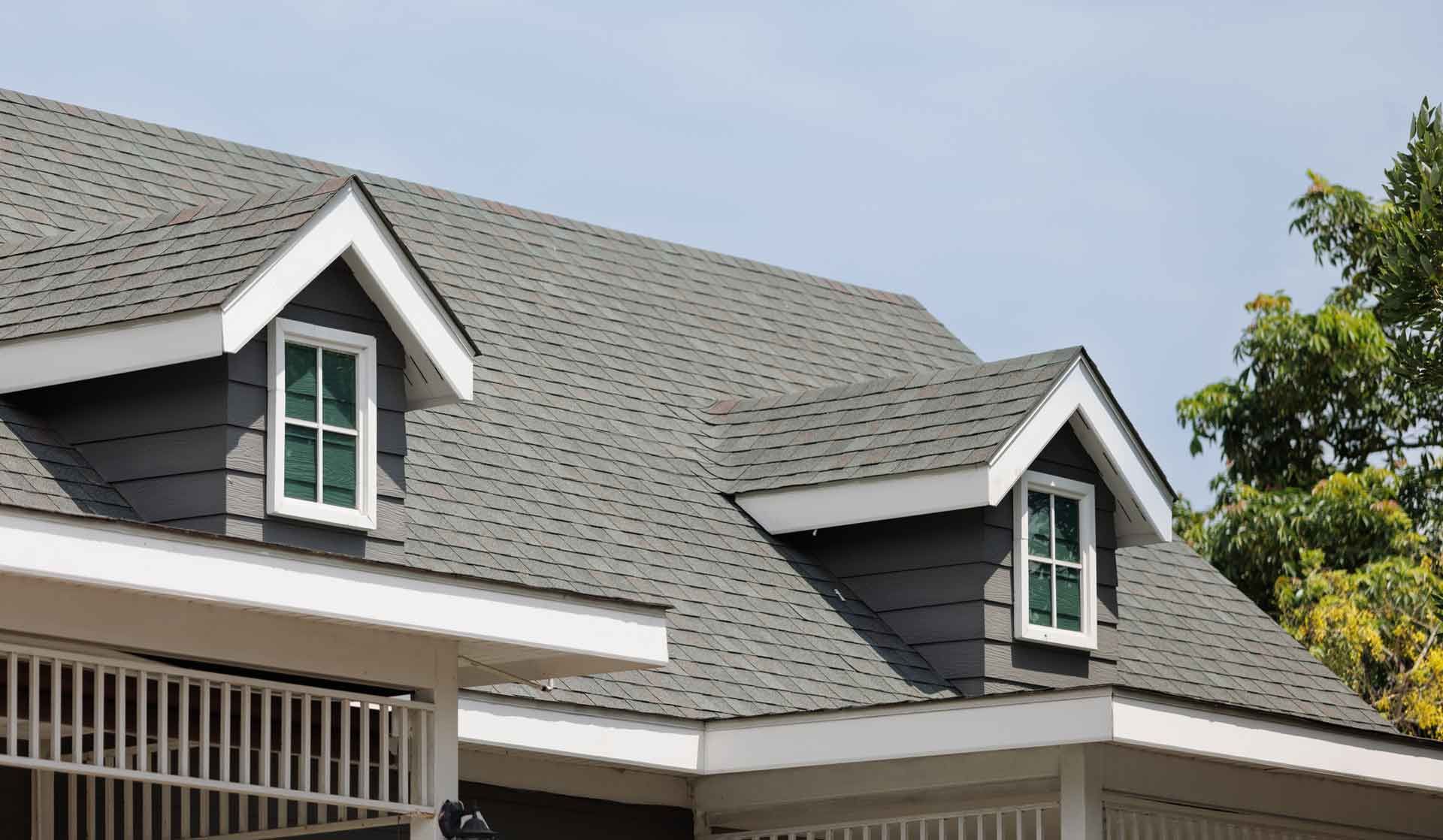 Gray roof with dormer windows on a house against a blue sky.