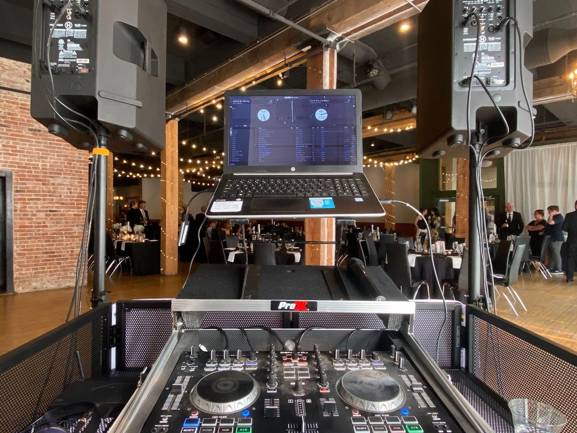 DJ setup with laptop and speakers at an event, with people in the background.