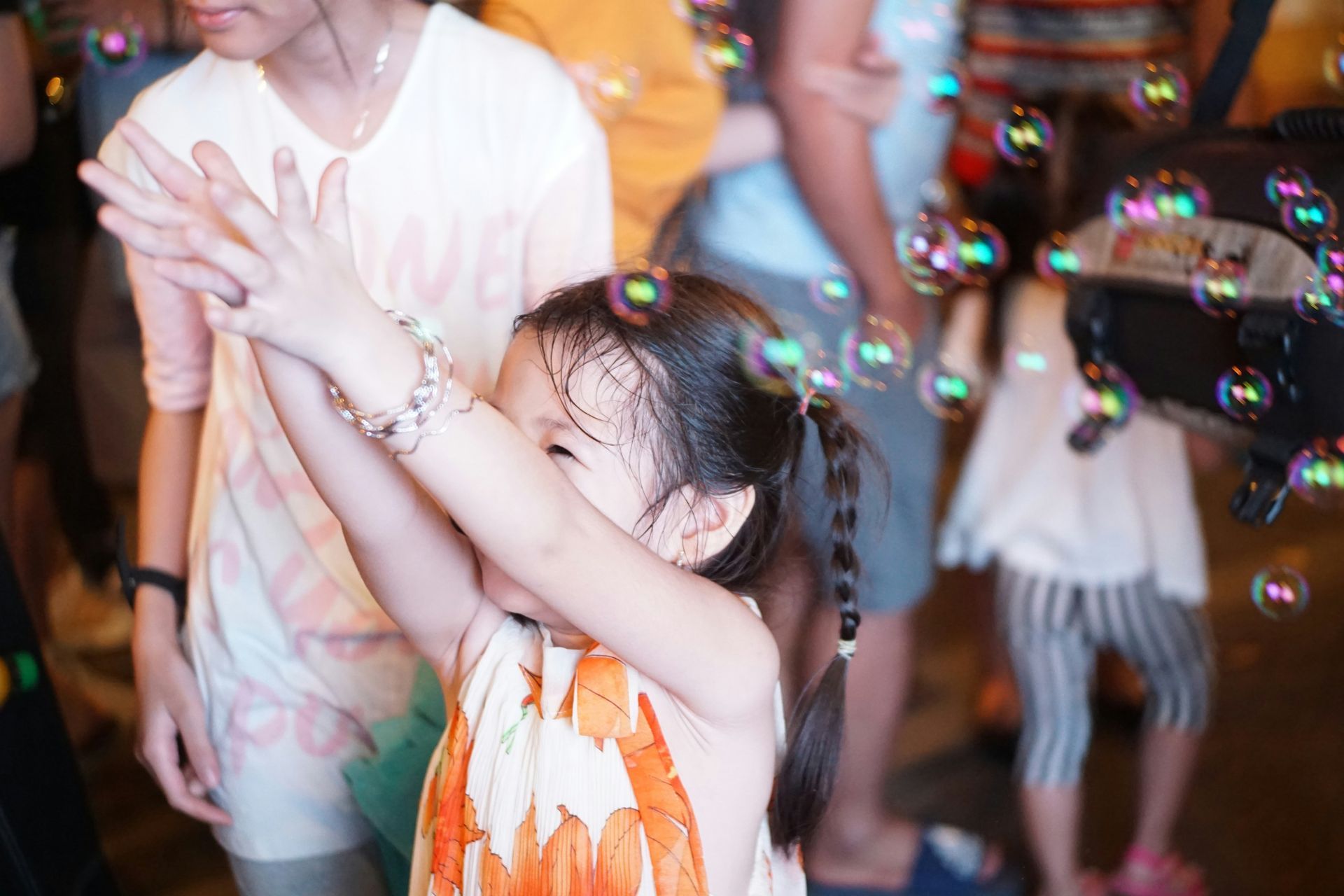 Young girl smiles with arms up, reaching for bubbles at a street event.