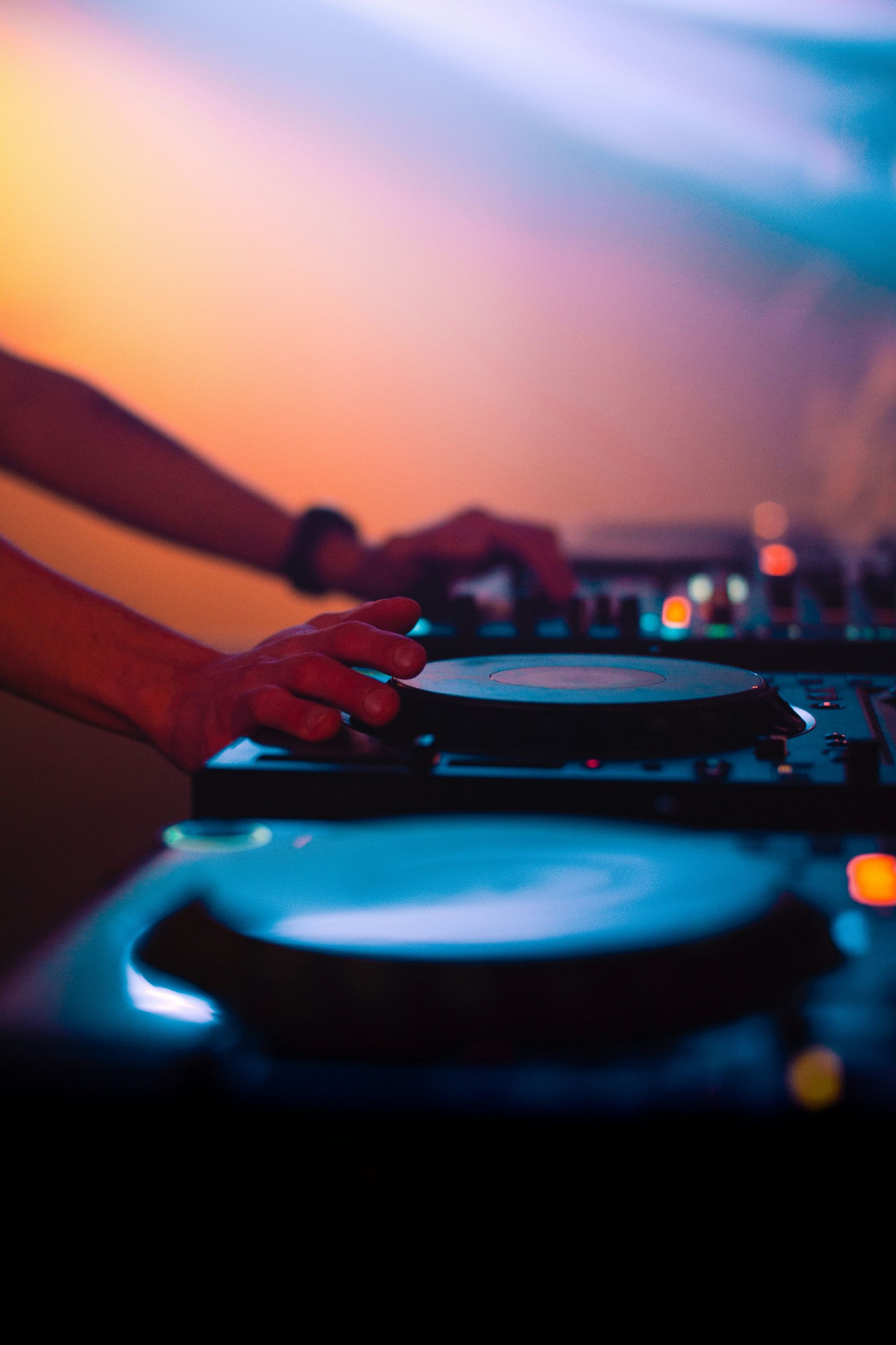 DJ's hands on turntables, mixing music at a club. Dark environment with blue and orange lighting.