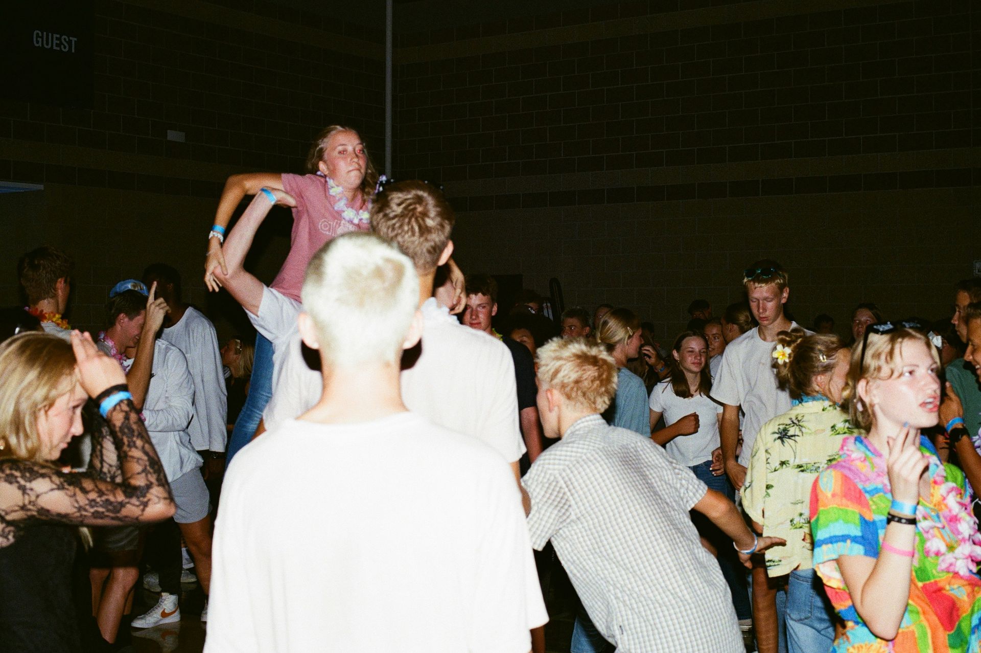 Party with a crowd of people; one is lifted up, others dance. Dim, indoor setting.