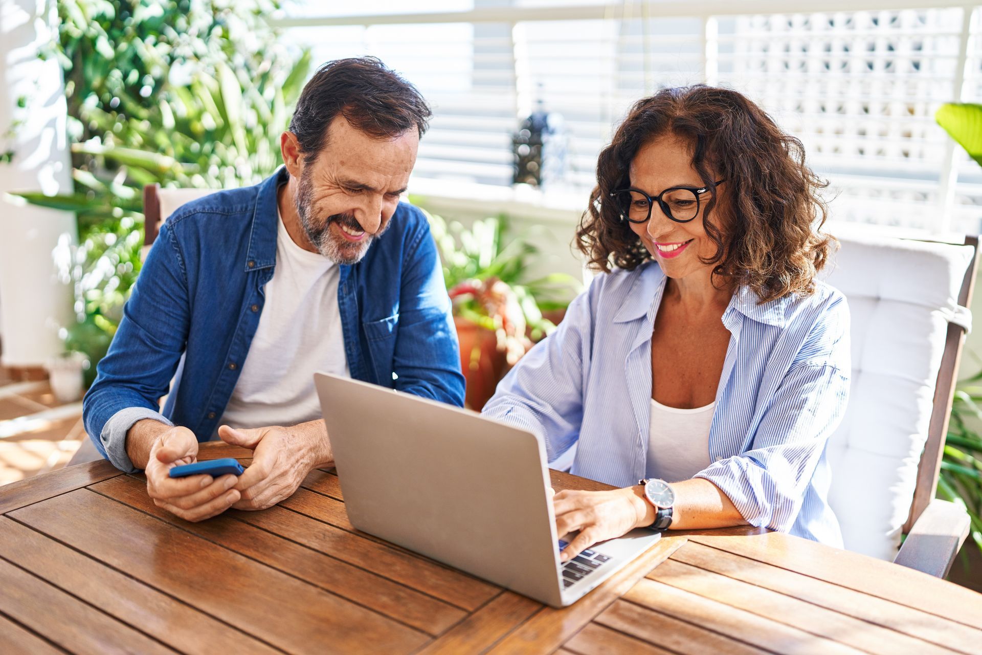 A man and a woman are sitting at a table looking at a laptop.