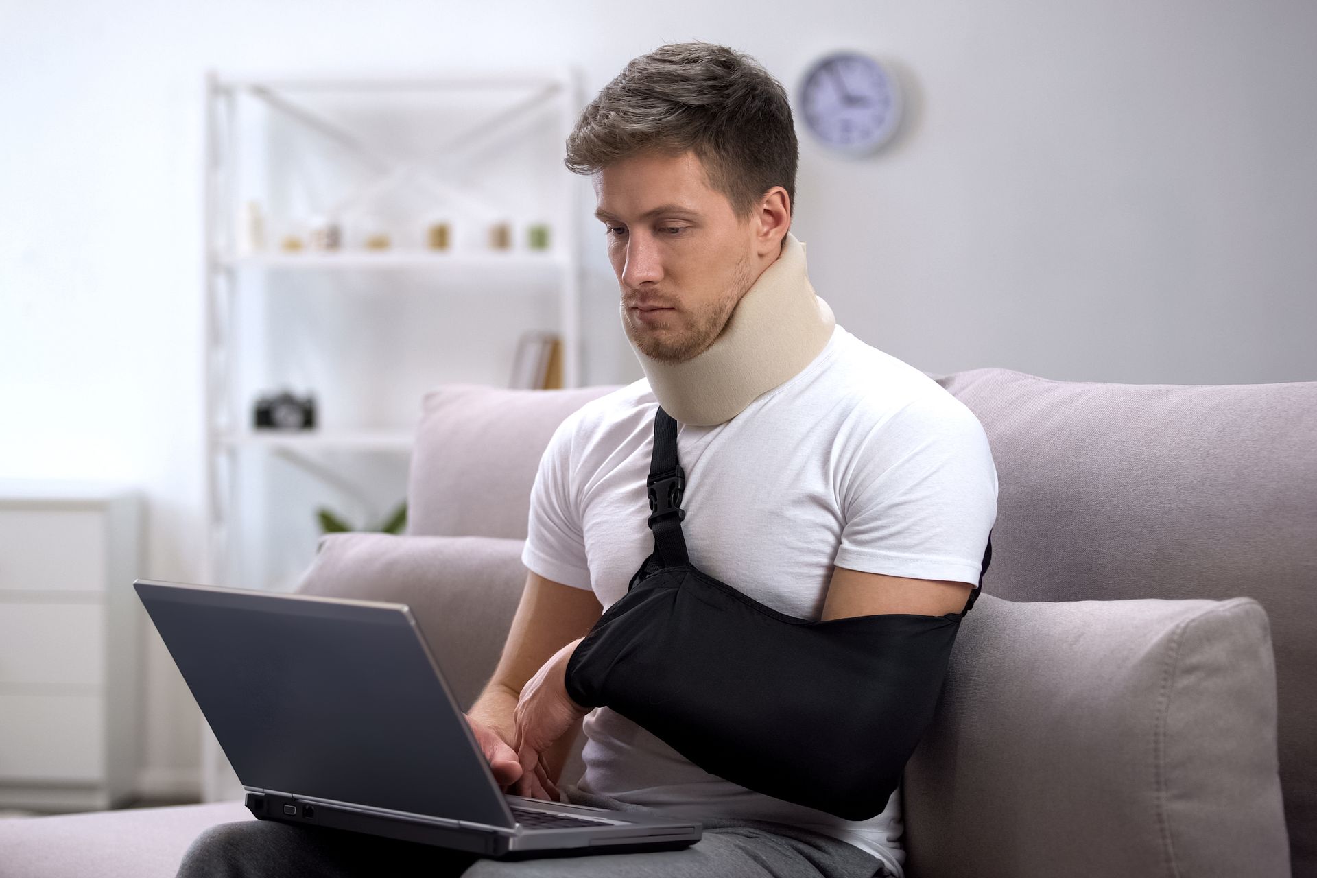 A man with a broken arm is sitting on a couch using a laptop computer.