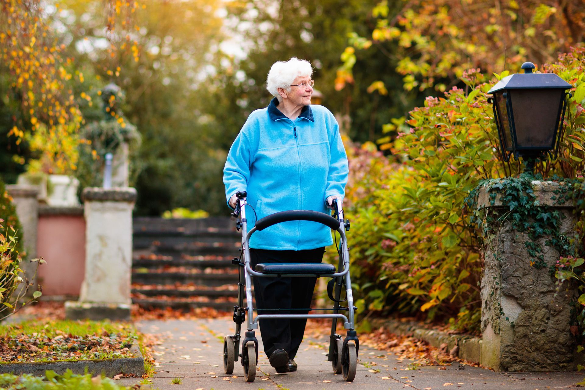 An elderly woman is walking with a walker in a park.