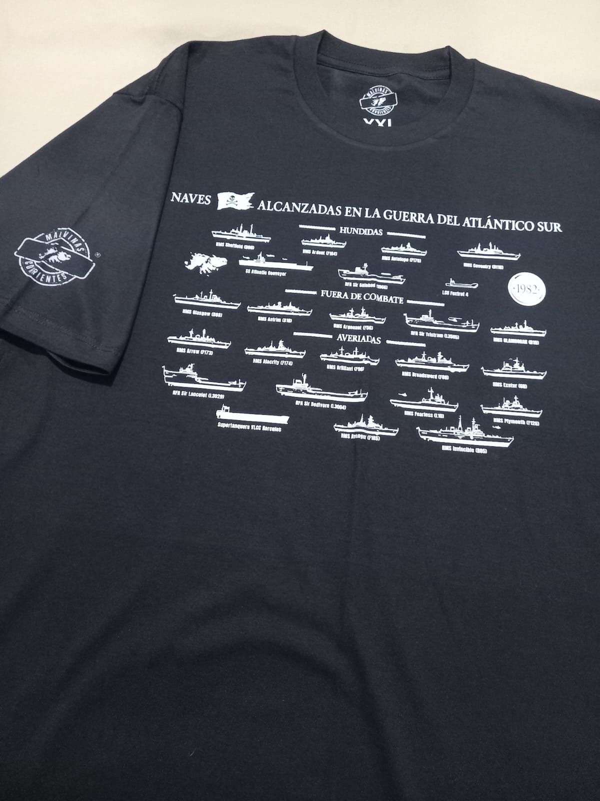 Camiseta negra con siluetas de barcos blancos y texto en español: «Malvinas, Atlántico Sur». Manga con logotipo.
