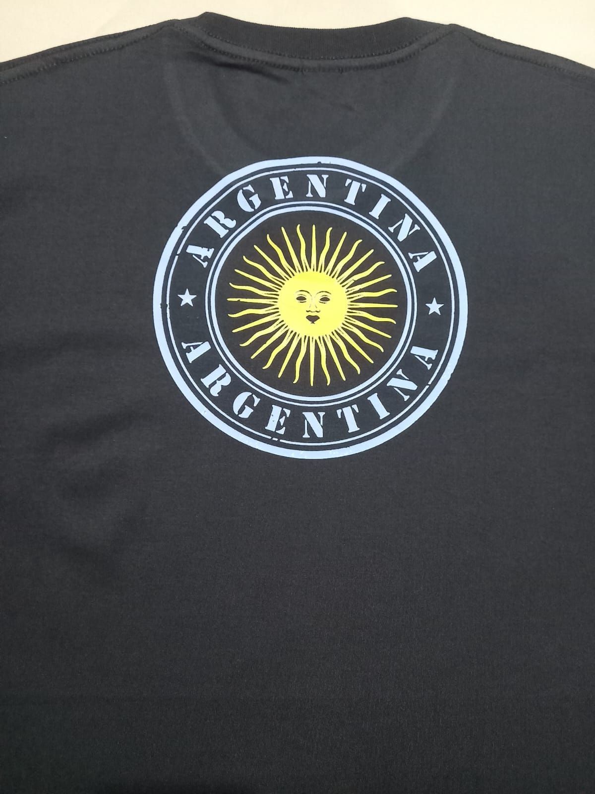 Camiseta negra con el emblema de Argentina: un sol sonriente en un diseño circular azul y blanco.