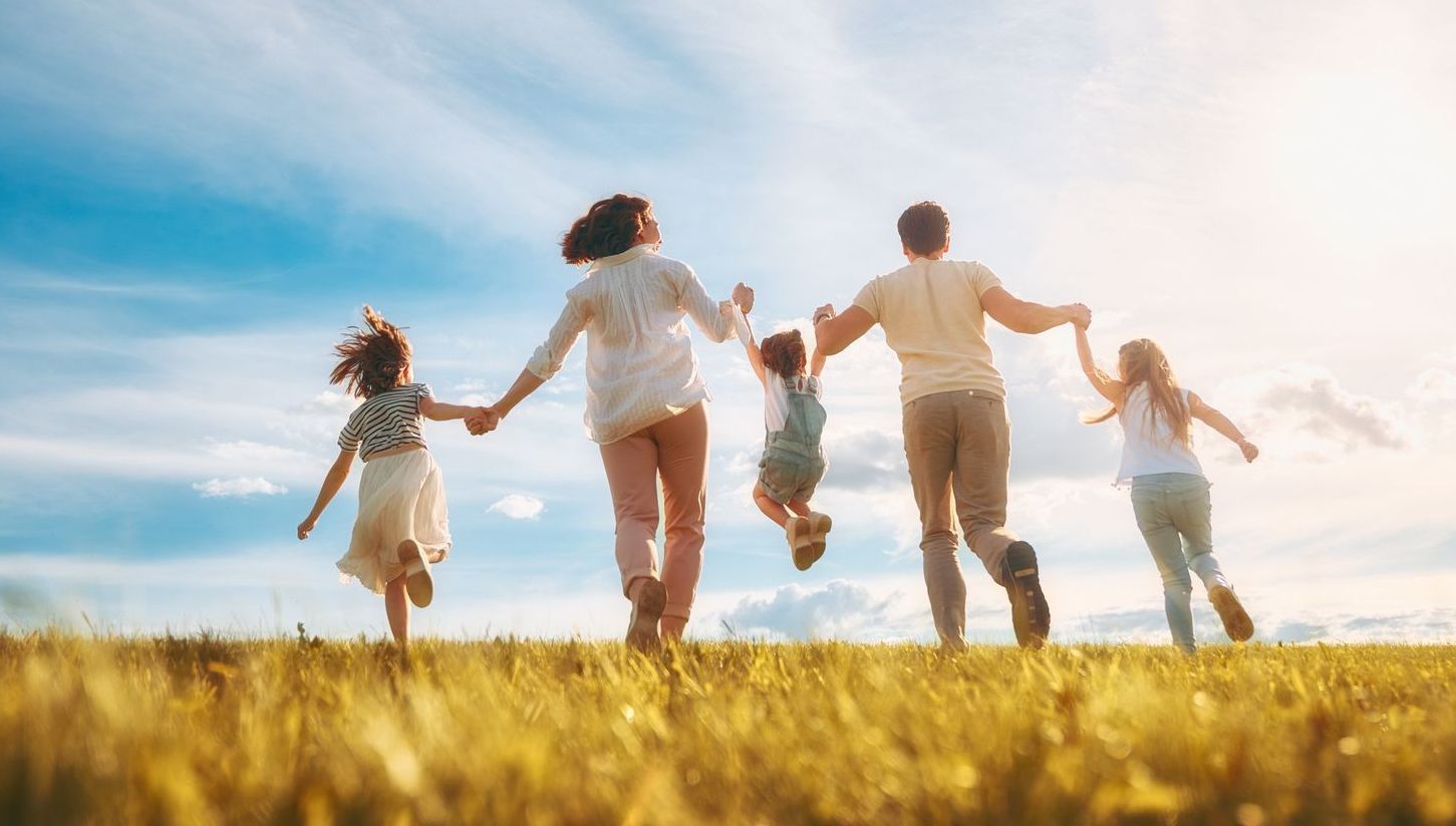Una familia se toma de la mano y corre por un campo.