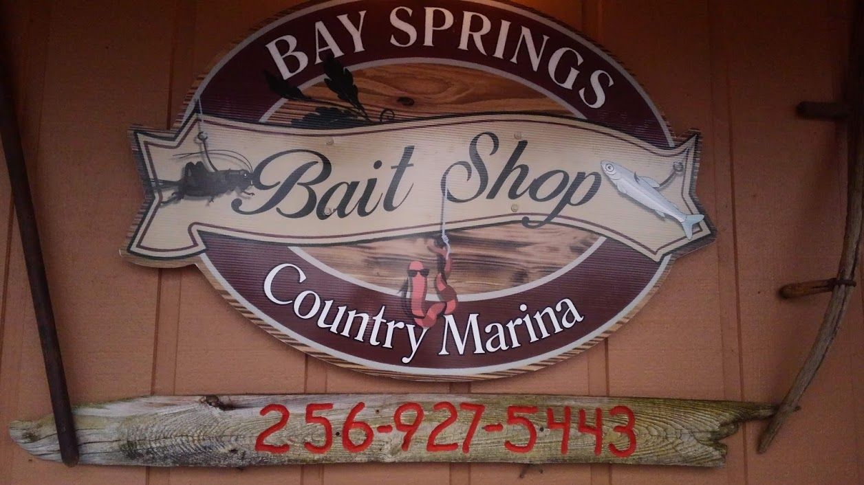 A sign for Bay Springs Bait Shop and Country Marina, with the phone number 256-927-5443, on a rustic wooden background.