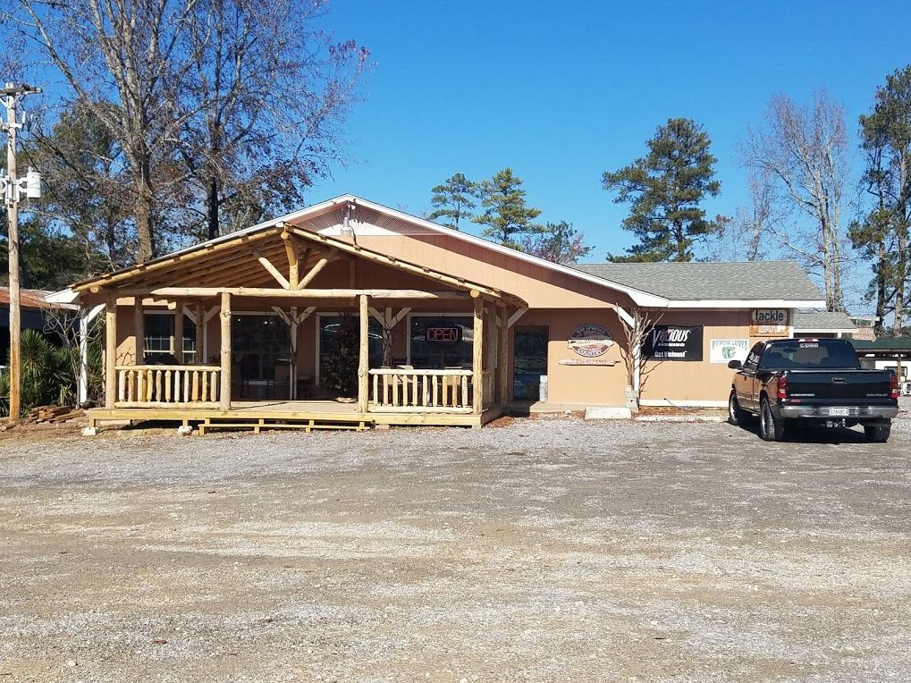A tan building with a large front porch and a black pickup truck parked on a gravel lot under a clear blue sky.