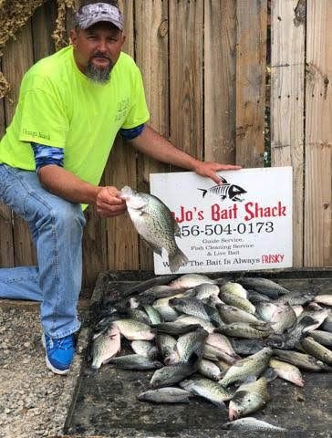 A person in a bright neon shirt kneeling next to a large pile of freshly caught fish and a bait shop sign.