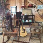A rustic room featuring a rocking chair, acoustic guitar, shelf with hats and toy trucks, and a small wooden chair.