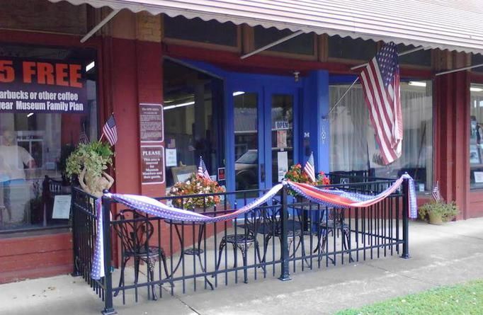 A storefront with a small outdoor patio enclosed by black iron fencing, decorated with red, white, and blue bunting.