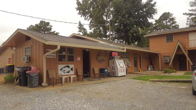 A brown, single-story building with a gravel parking lot, an ice machine, and outdoor seating near the entrance.