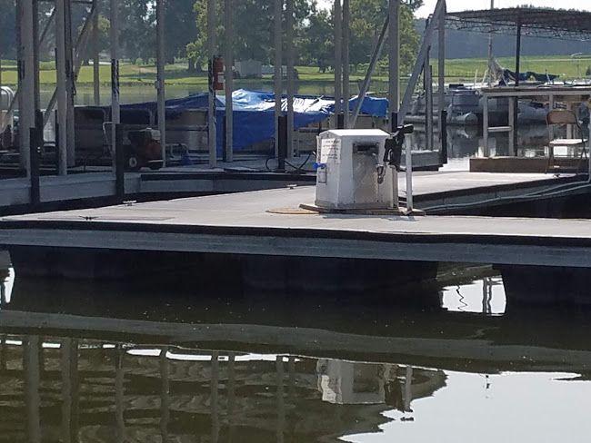 A floating boat dock on a calm lake, featuring a white power pedestal and covered boat slips in the background.