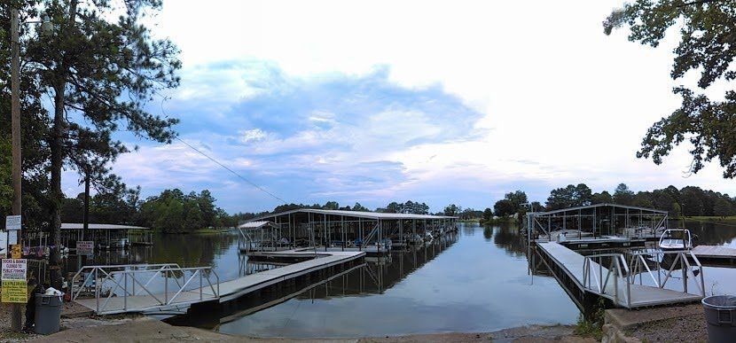 Panoramic view of a marina with covered boat slips, wooden docks, and calm water under a cloudy sky.