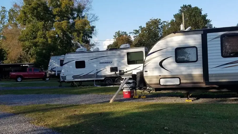 Several travel trailers are parked in a gravel campground during the day, with a red truck visible in the background.
