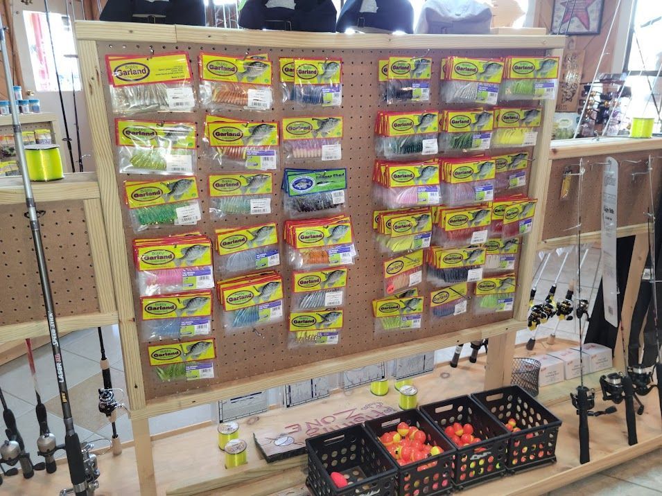 A pegboard display in a tackle shop featuring various packaged fishing lures and plastic baskets of colorful bait.