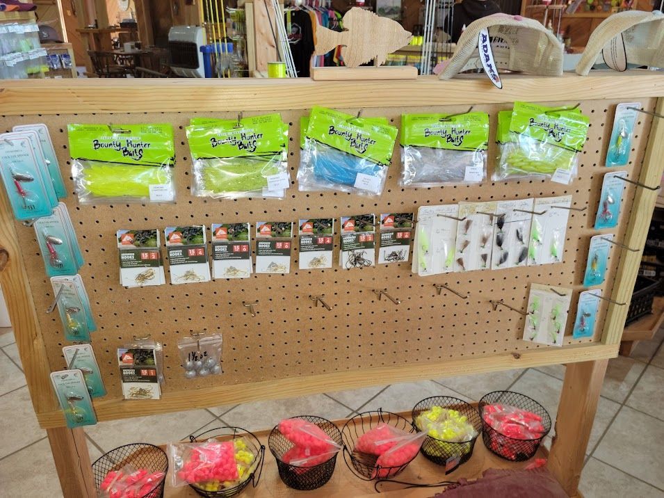 A pegboard display in a retail store filled with various fishing lures, plastic baits, and hooks for sale.