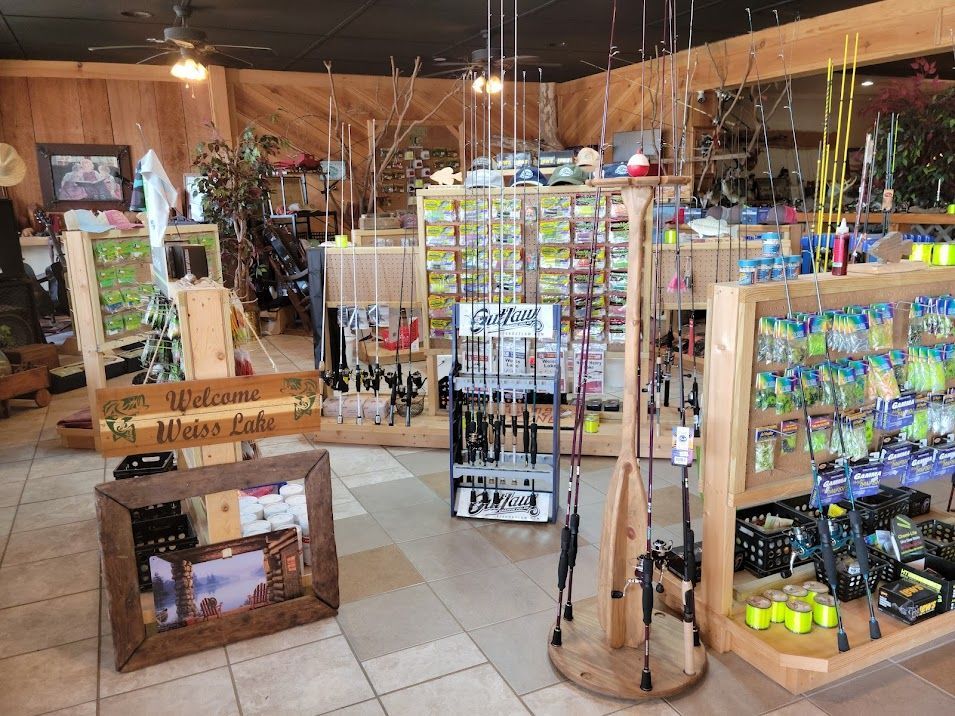 Inside a fishing gear store, rows of wooden shelving display various rods, lures, and tackle for sale.