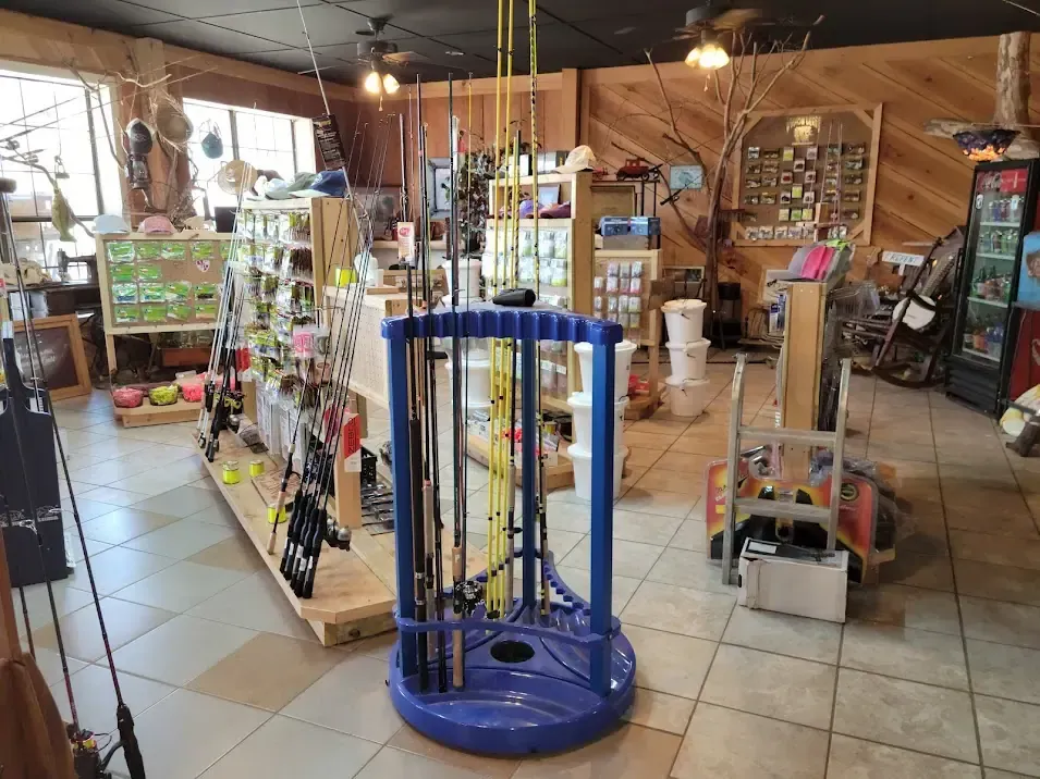 A fishing tackle shop with various rods displayed in a blue, circular stand, surrounded by shelves of sporting goods.
