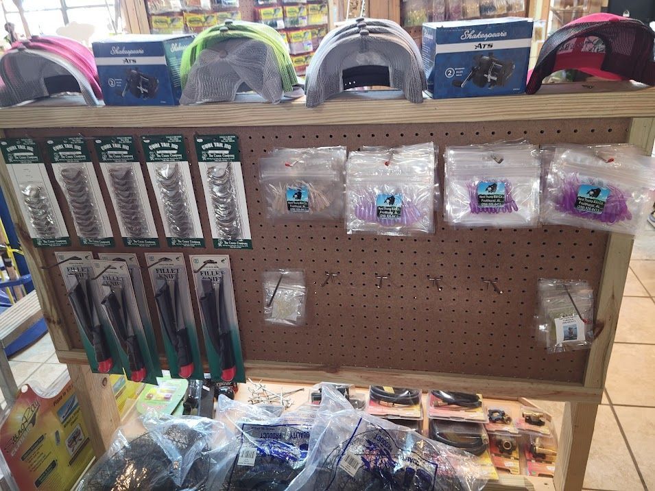 Retail display featuring fishing caps, boxes of fishing equipment, and various packaged lures on a pegboard wall.
