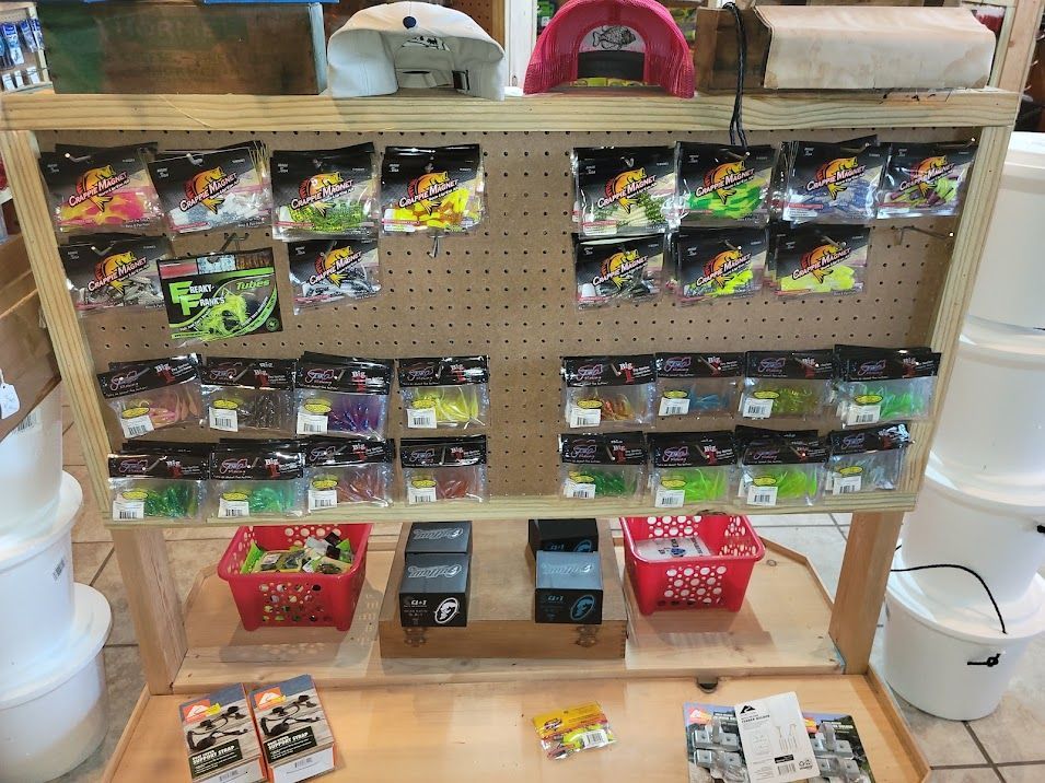 A pegboard display in a store featuring multiple packages of colorful plastic fishing lures and two red plastic baskets.