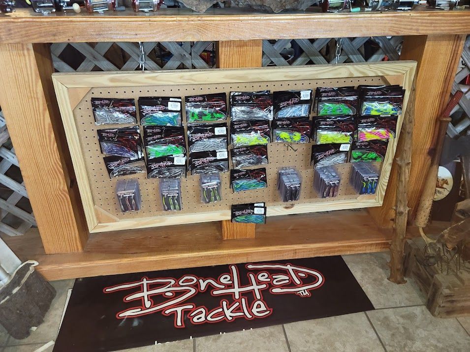 Pegboard display of various colorful fishing lures and soft plastics inside a wooden frame, labeled Bonehead Tackle.