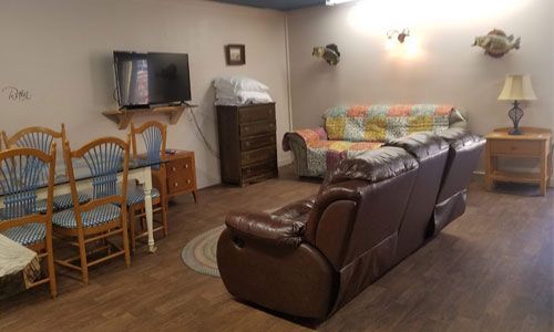 A room with a brown leather couch in the foreground, a floral sofa, dining table, and a TV mounted on the wall.