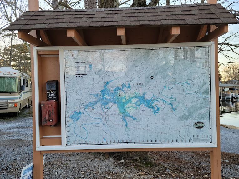 A map of a lake inside a wooden display case, located outdoors near a parked recreational vehicle.