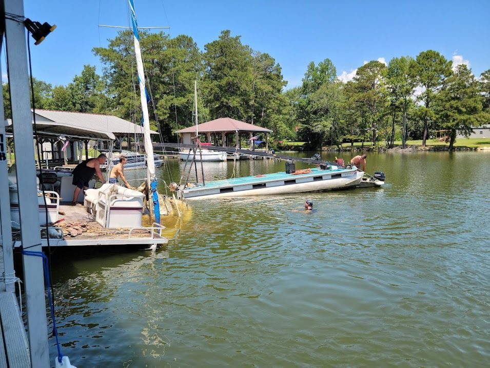 People working on a pontoon boat docked at a lake pier on a sunny day.