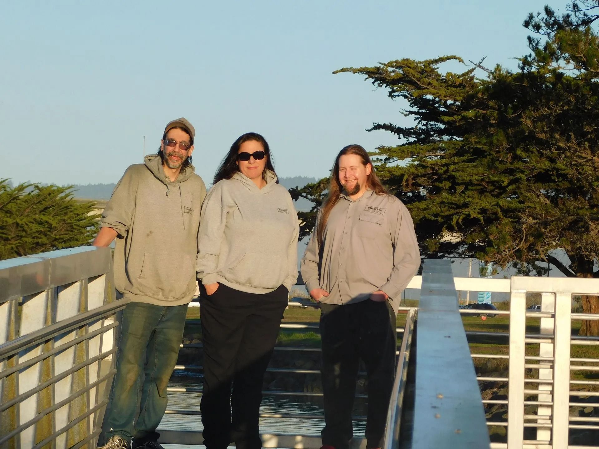 Three people standing on a bridge wearing grey sweatshirts