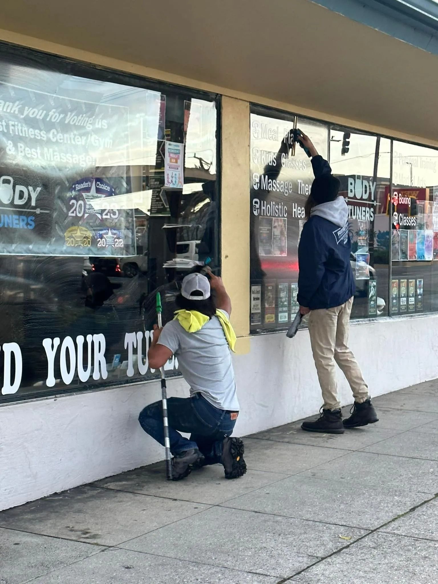Two men are cleaning the windows of a store.