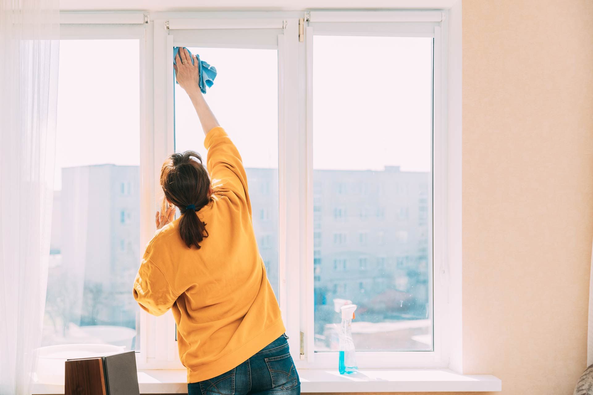 A woman is cleaning a window with a cloth in a living room