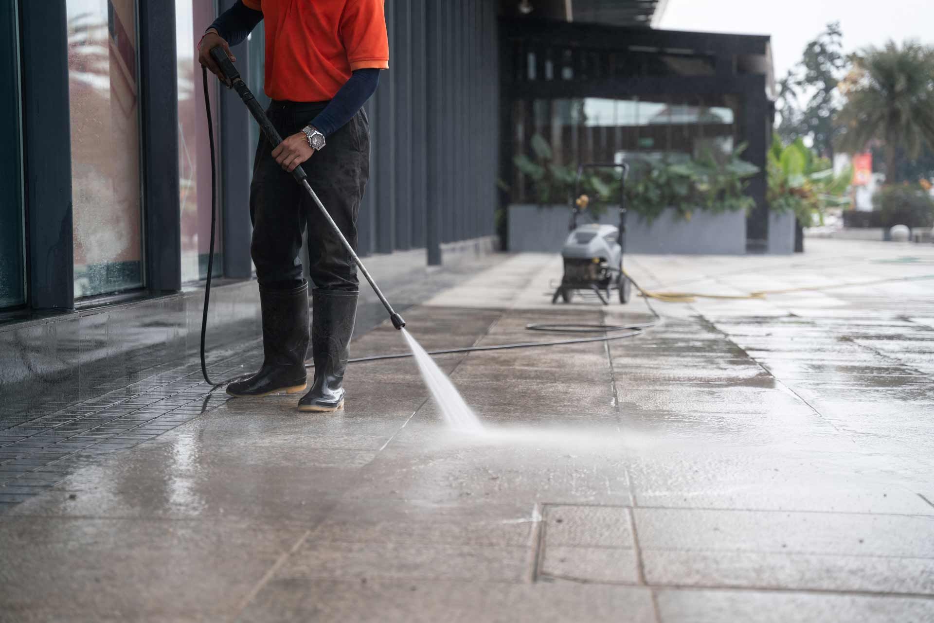 A man is using a high pressure washer to clean a sidewalk