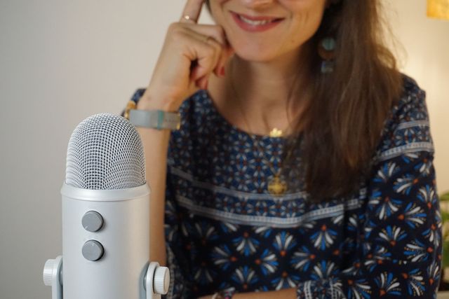 Frau lächelt neben einem silbernen Mikrofon, blaues gemustertes Hemd.