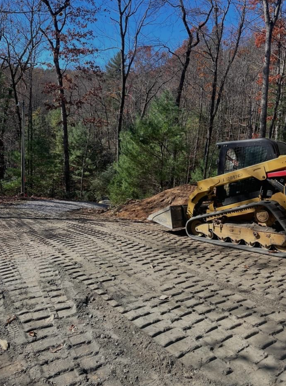 A bulldozer is driving down a dirt road in the woods.