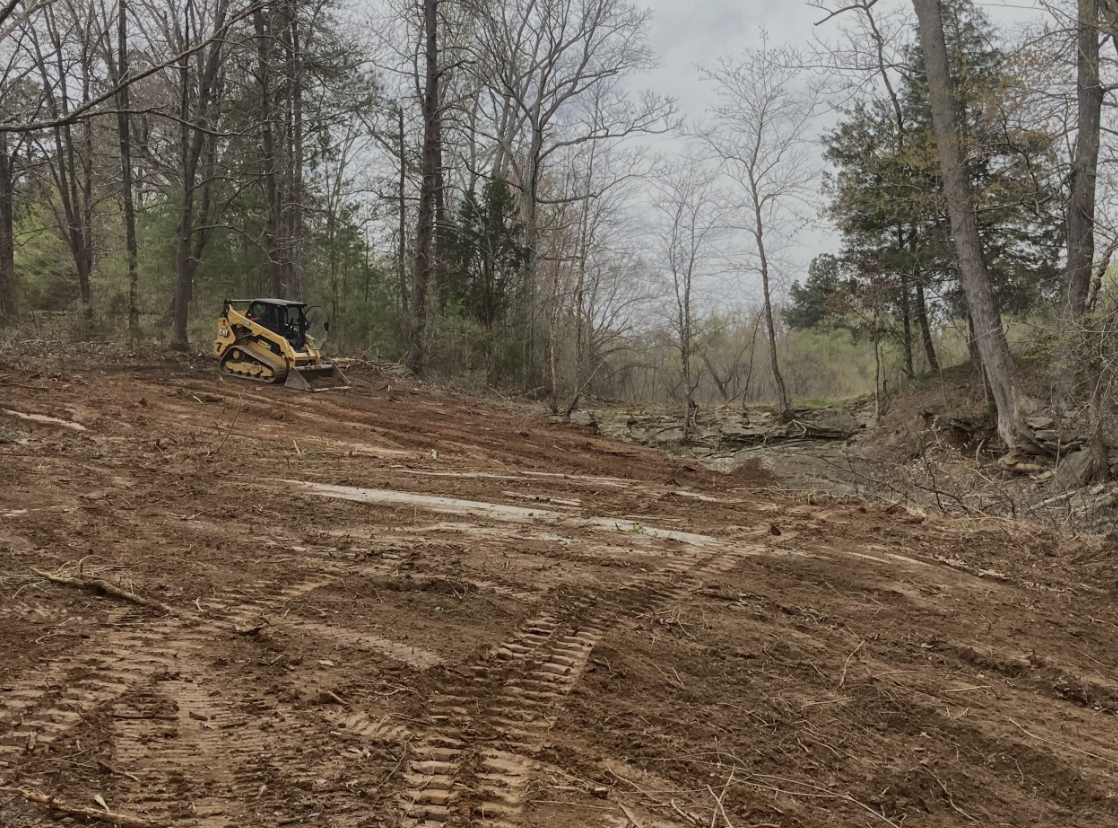 A bulldozer is working on a dirt road in the woods.