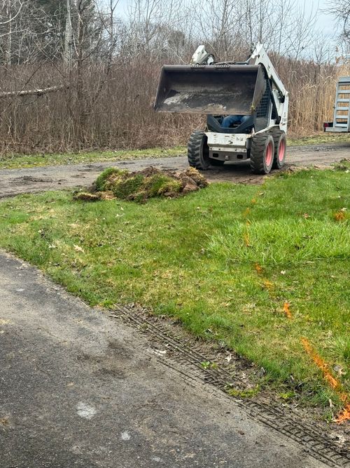 A bobcat is driving down a dirt road next to a grassy field.