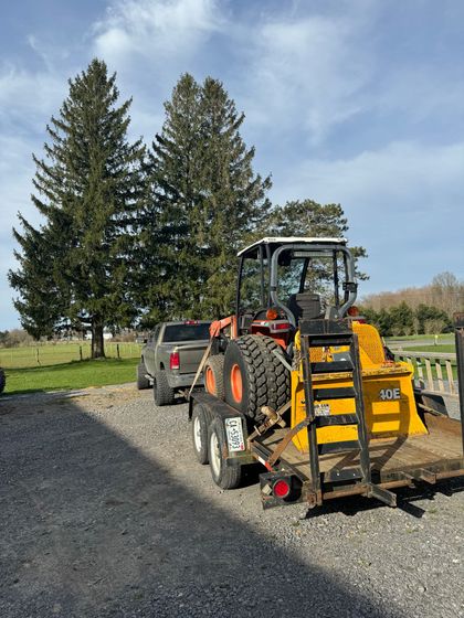 A tractor is being towed by a truck on a trailer.