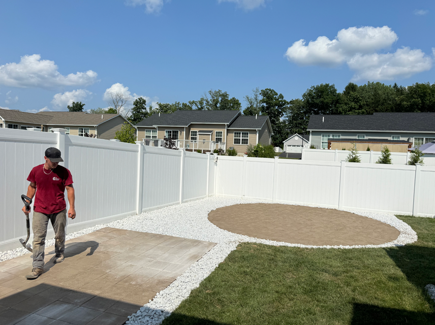 A man is walking through a backyard with a white fence.